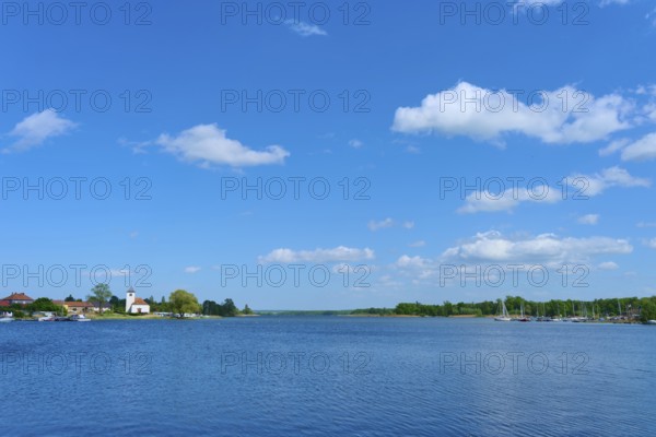 Lake with blue sky and clouds, in the background a village with a church, Rhodes, Etang du Stock, Sarrebourg, Moselle, France