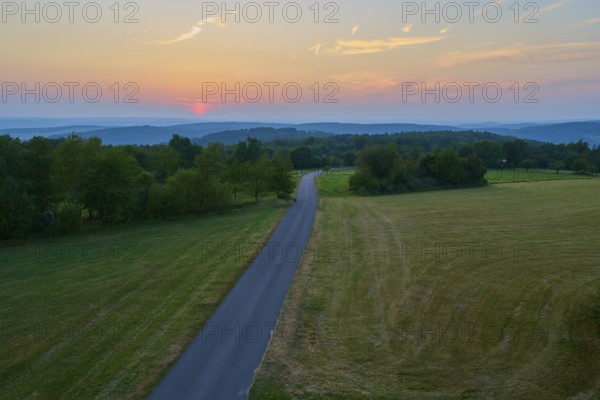 Narrow road winds through fields at sunset with orange sky, Geishöhe, Dammbach, Spessart, Bavaria, Germany
