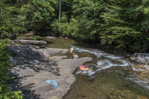 Senior couple watches children floating down the Hiawassee River on inflatable rafts near Hayesville, North Carolina, USA