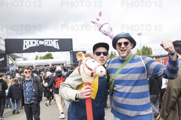 Two festival visitors with their inflatable animals Charles and Chantal in front of a container with the Rock am Ring logo at the Rock am Ring Festival on Friday, Nürburgring race track race track, 06/06/2025