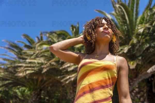 Young woman enjoying music with headphones in a tropical location, embracing the summer vibes and relaxing under palm trees