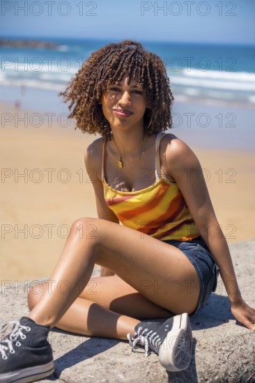 Young woman with curly hair sitting on a beach wall, enjoying the sunny weather and ocean view