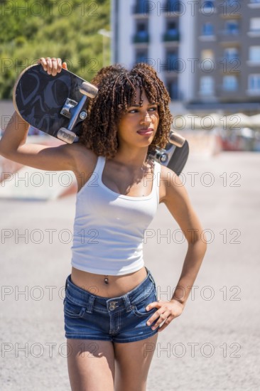 Confident young woman holding skateboard on shoulder, enjoying urban lifestyle and skateboarding culture