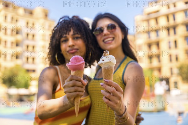 Two young women smiling brightly while holding colorful ice cream cones on a sunny summer day in the vibrant city, enjoying their time together