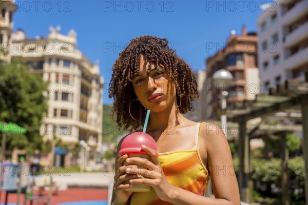 Fashionable young woman enjoys a cold beverage in a vibrant urban setting, embracing the summer vibes