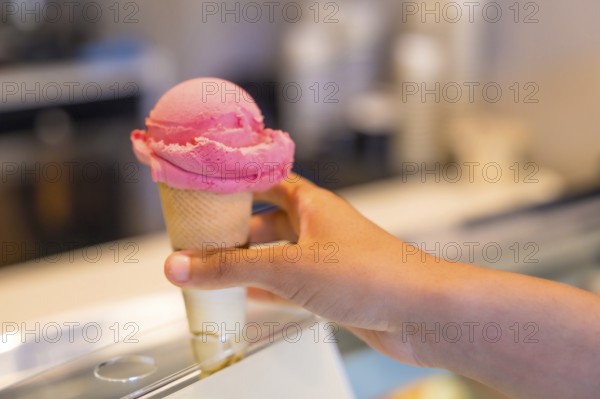 Customer selecting a delightful pink ice cream cone from a well stocked refrigerated display case in a charming gelateria