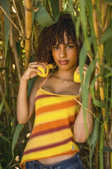 Young woman holding vibrant yellow headphones while posing gracefully in a lush bamboo forest, surrounded by serene greenery and natural beauty