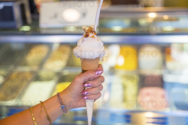 Woman enjoying a delicious ice cream cone with toppings, inside a gelateria with a display case full of colorful frozen desserts