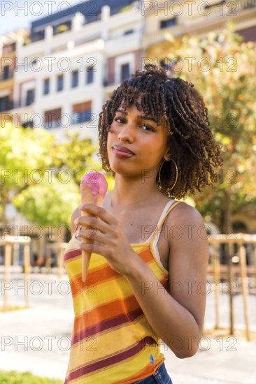 Stylish young woman savoring a refreshing strawberry ice cream cone on a sunny day in the city