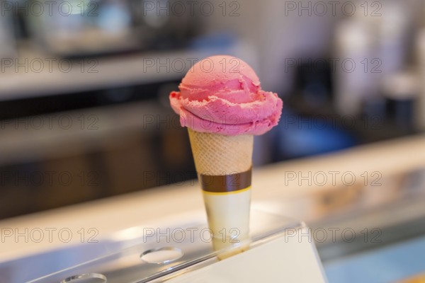 Refreshing pink ice cream scoop melting on crispy cone, displayed on showcase in ice cream shop, ready to be served