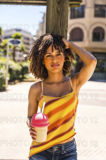 Fashionable young woman enjoying a sunny day in the city, holding a refreshing beverage and radiating happiness while relaxing outdoors