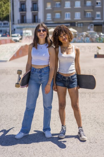Two young women skaters posing with their skateboards at a vibrant skate park, enjoying the sunny day and embracing their active lifestyle