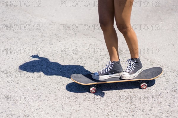 Close up of legs balancing on a skateboard, casting a striking shadow on the asphalt under bright summer sunlight