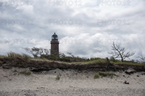 Lighthouse behind sand dune with sparse vegetation and dramatic cloudy sky, Prerow, Mecklenburg-Vorpommern, Germany