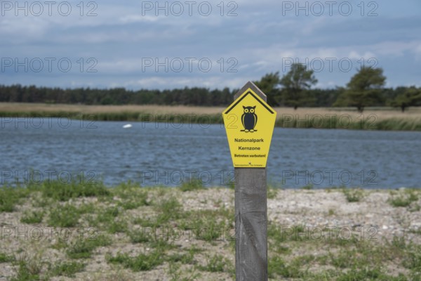 Yellow national park sign with owl in the foreground, water and cloudy sky in the background, Prerow, Mecklenburg-Vorpommern, Germany