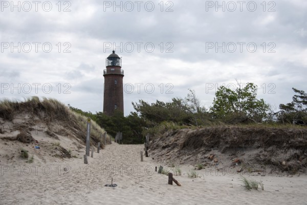 Path through sand dunes leads to the Darßer Ort lighthouse, surrounded by nature and cloudy skies, Prerow, Mecklenburg-Vorpommern, Germany