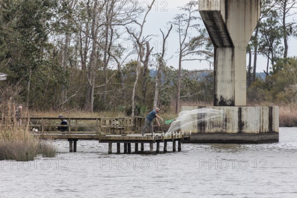 Man throwing cast net off end of wooden pier under a bridge near Fairhope, Alabama, USA