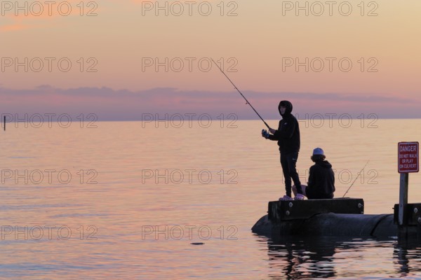Silhouette of young adults ignoring danger sign while fishing on storm drain culvert in Long Beach, Mississippi, USA