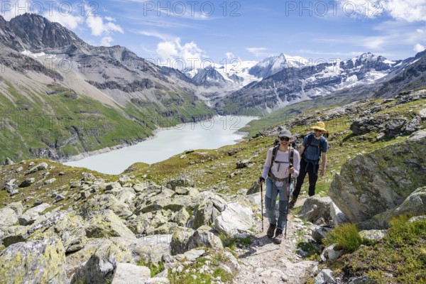 Mountaineer on a hiking trail at a blue mountain lake, reservoir Lac des Dix, behind mountain peak Mont Blanc de Cheilon, Hérménence, Valais Alps, Valais, Switzerland