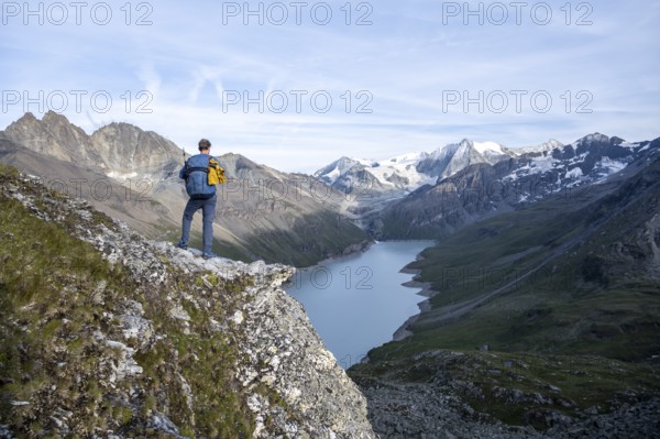 Mountaineer on the summit of Mont de la Blana, view of a blue mountain lake, Lac des Dix reservoir, behind mountain peak Mont Blanc de Cheilon with glacier, Hérménence, Valais Alps, Valais, Switzerland