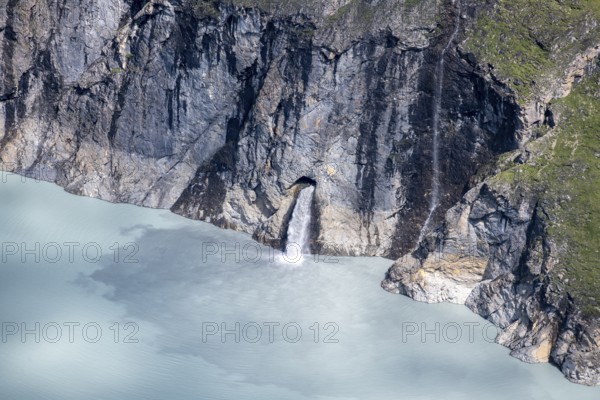 Waterfall cascades from a rock face into a blue mountain lake, Lac des Dix reservoir, Valais Alps, Valais, Switzerland