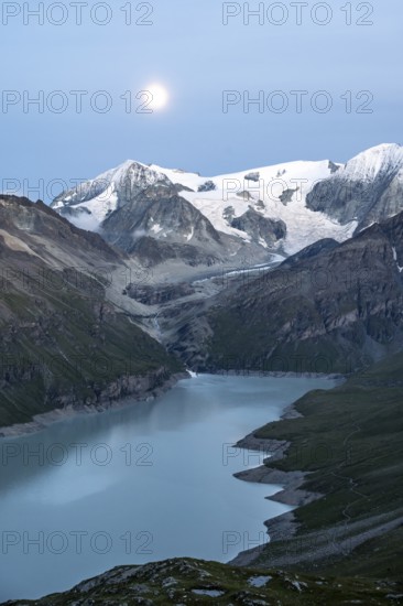 Mountain landscape with turquoise blue reservoir Lac des Dix and summit Mont Blanc de Cheilon, evening mood, moon stands above mountain peaks at the blue hour, Hérménence, Valais Alps, Valais, Switzerland