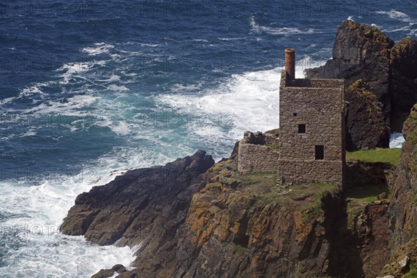 An old stone house perched on cliffs above a stormy sea with crashing waves, engine room, mining, Botallack, Cornwall, England, United Kingdom
