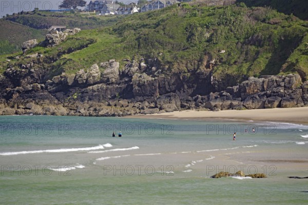 Small waves rolling towards a sandy beach with rocks, people enjoying the water, St Ives, Cornwall, England, United Kingdom
