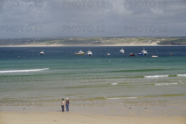 Boats anchored on calm waters off a wide, deserted sandy beach, St Ives, Cornwall, England, United Kingdom