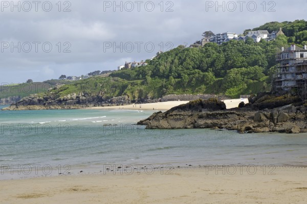 Sandy beach beach with sea view and hills covered with green trees and scattered houses, St Ives, Cornwall, England, United Kingdom