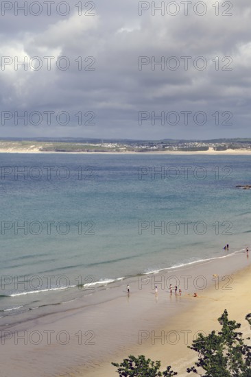 Several people walking on a quiet sandy beach, the sea under a cloudy sky, St Ives, Cornwall, England, United Kingdom