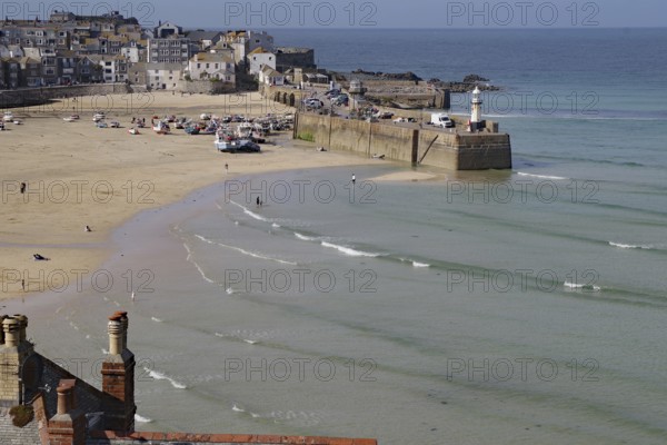 Coastal town with harbour and lighthouse, boats on the beach and gentle waves in the blue sea, tides, St Ives, Cornwall, England, Great Britain