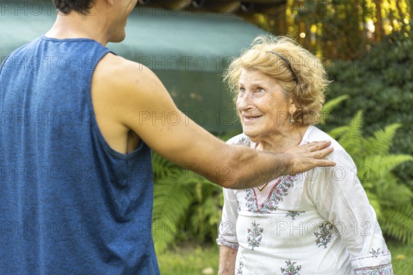 Young physiotherapist supporting and comforting smiling elderly woman during rehabilitation session in a garden, promoting health and wellbeing in old age