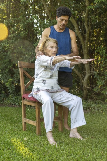 Senior woman practicing seated stretches with the assistance of a physiotherapist in a peaceful outdoor setting, promoting mobility and well-being