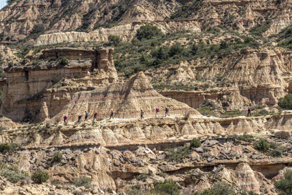 Group of hikers at colorful sandstone rock formations, desert, along gravel road Ruta Jubierre, Desierto de los Monegros, Spain