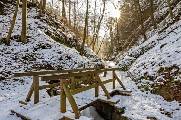 Wooden bridge over a snow-covered path in a sunny winter forest, The Dragon Gorge near Eisenach in Thuringia