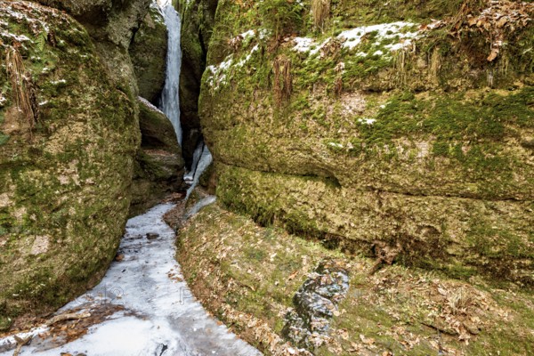 Narrow pass between moss-covered rocks with dammed ice and snow-covered ground, the Dragon Gorge near Eisenach in Thuringia