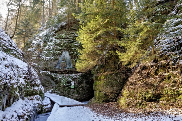 Snow-covered forest path leads through a shady gorge with rock-like formations and moss, The Dragon Gorge near Eisenach in Thuringia