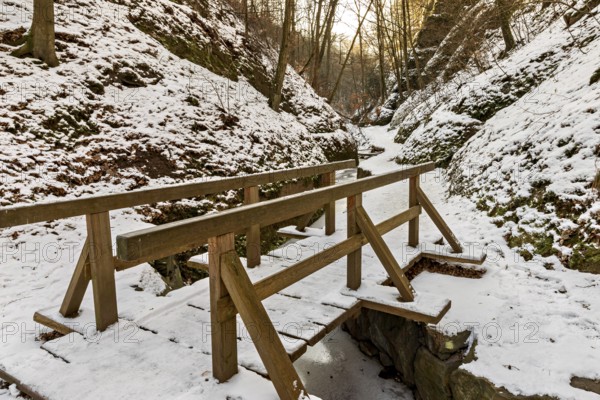 Narrow wooden bridge over a frozen stream in a snowy forest gorge at sunset, The Dragon Gorge near Eisenach in Thuringia