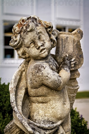 Weathered stone statue of an angel child with wings and background outdoors, stone statues in the town of Kempten im Allgäu