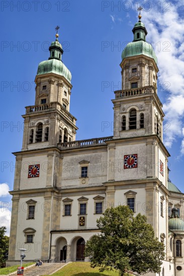 Baroque church with two towers and clocks against a blue sky, surrounded by trees, The town of Kempten im Allgäu
