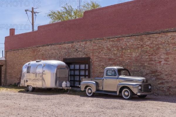 Silver painted classic fort pickup truck and a stainless steel Airstream camper travel trailer parked in downtown Winslow Arizona