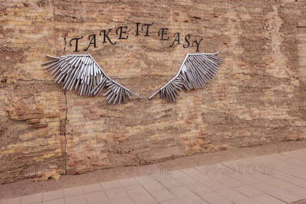 Metal tubular art on brick wall for tourists to pose for pictures at Standin' on the Corner Park in downtown Winslow, Arizona