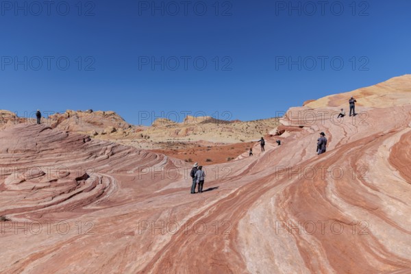 Hikers on a layered sandstone rock formation in the Fire Wave area of Valley of Fire State Park near Overton, Nevada