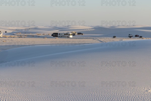 Cars and RVs in a parking area behind a rippled white gypsum sand dune at White Sands National Park in Alamogordo, New Mexico, USA