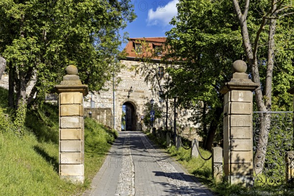Entrance gate to the castle, flanked by stone pillars and trees, under a bright blue sky, The Creuzburg in Thuringia