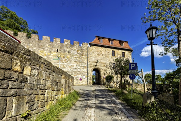 Stone entrance to a castle with cobblestone street and blue sky in the background, The Creuzburg in Thuringia
