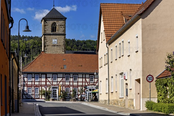 Church tower towers above half-timbered house and village street in sunny weather, The church tower of the Protestant church in Creuzburg in Thuringia