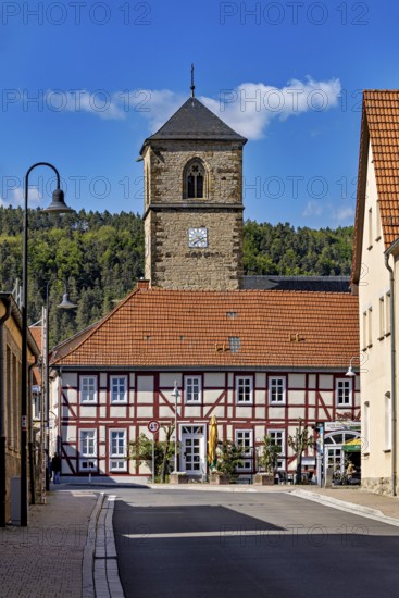 A half-timbered house with a church tower in the village, shining under a blue sky, The church tower of the Protestant church of Creuzburg in Thuringia