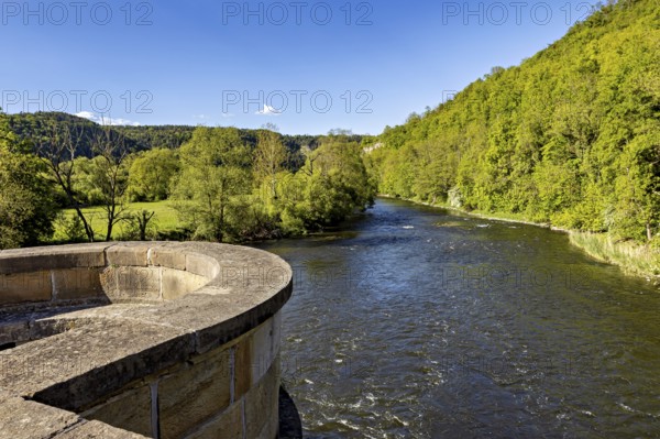River next to a stone bridge, surrounded by forest under a blue sky, view from the historic Werra bridge over the Werra to the Ebenauköpfen near Creuzburg in Thuringia